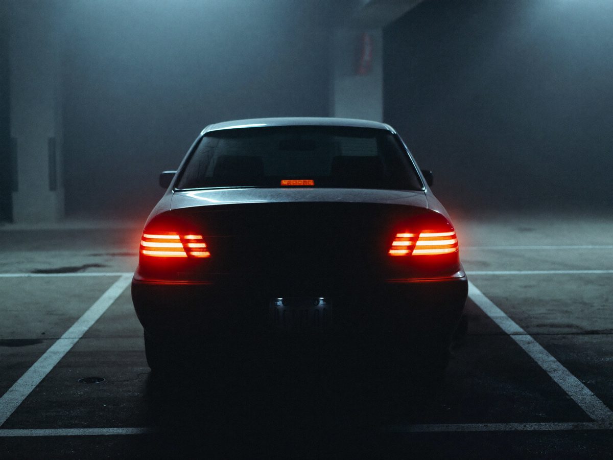 The rear of a dark sedan with heavily tinted glass, tail lights glowing in a night car park