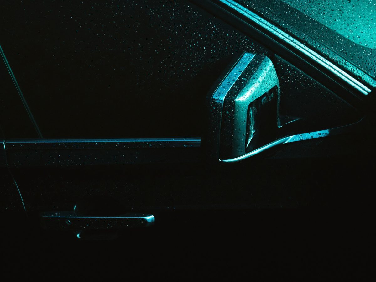 Close-up of a tinted car window beaded with rain at night