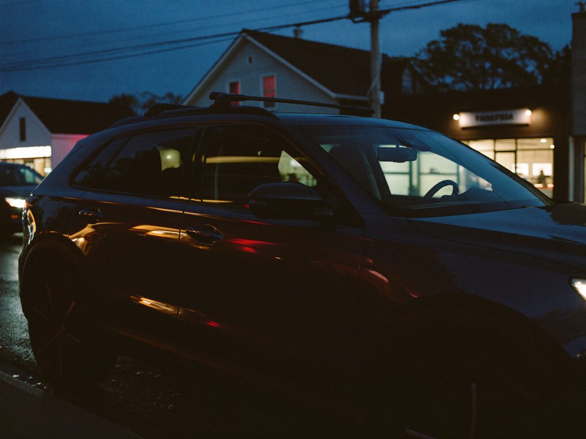 A dark SUV with tinted windows parked on a small-town main street at dusk