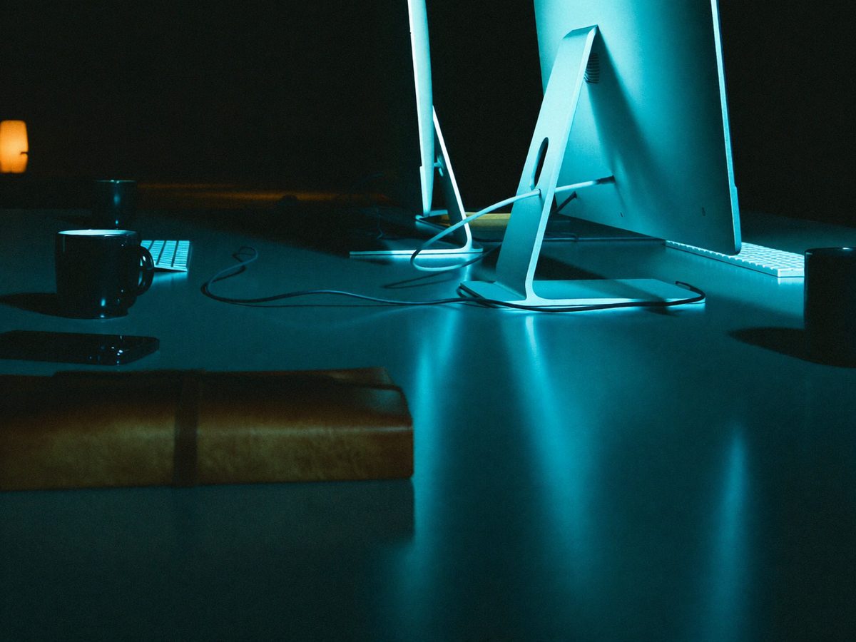 A dark desk at night lit by the cyan glow of monitors
