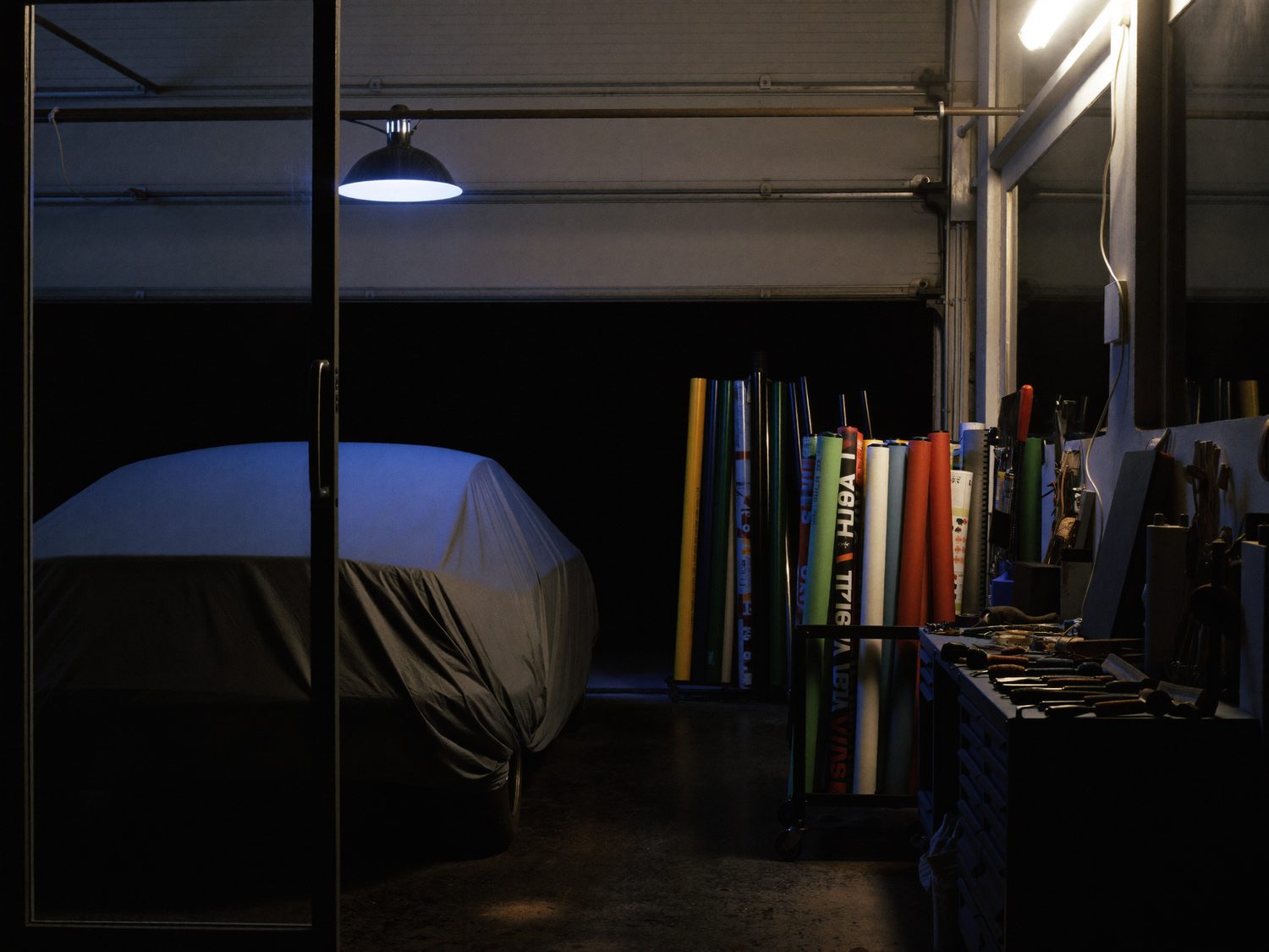 A dark tint shop at night with rolls of film on a rack and tools laid out on the bench